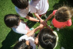 Top-view of children joining hands as a team in a sunny park, promoting unity.